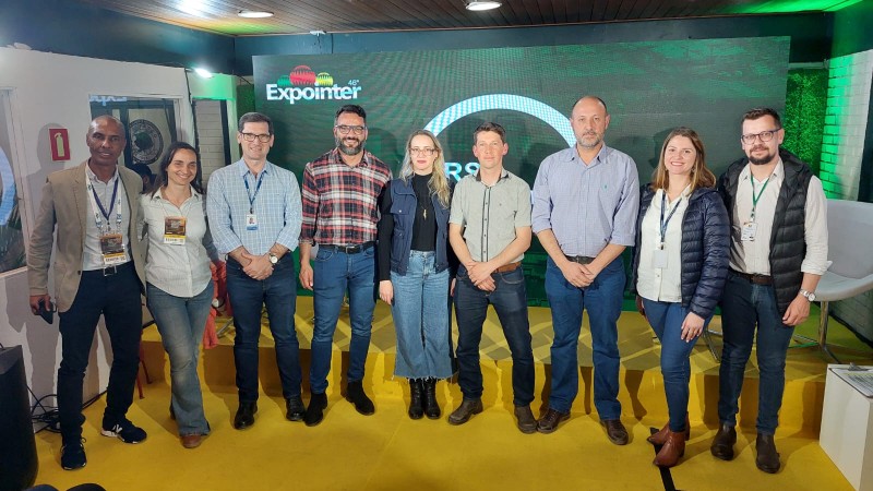 No estande do RS Innovation Agro, grupo de representantes do grupo de trabalho do projeto "Conecta Rural" posa para foto diante de painel verde com o logo do estande.